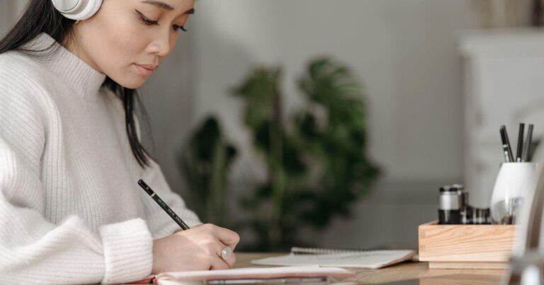 Người đeo tai nghe ghi chép vào sổ tại bàn; ảnh stock minh họa hoạt động nghe và ghi chú.